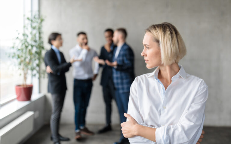 Des collègues masculins chuchotent dans le dos d'une femme d'affaires mécontente au bureau